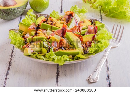 Avocado salad with fried bacon and pine nuts on a white wooden background