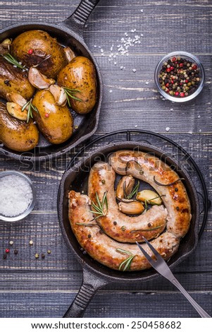 Country style potatoes and fried sausages with rosemary, garlic on a wooden dark background