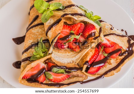 Homemade Crepes with strawberries and chocolate syrup on a white background