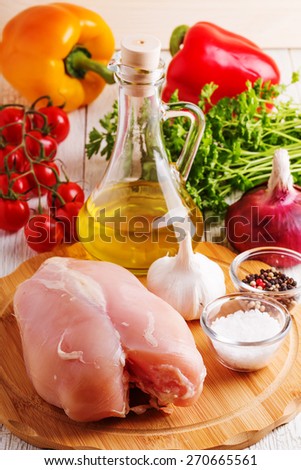 Raw chicken breasts on a cutting board with vegetables, spices and olive oil.