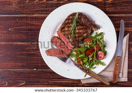 Ribeye steak with arugula and tomatoes on  dark wooden background.