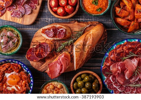 Typical spanish tapas concept. Concept include variety slices jamon,  chorizo, salami, bowls with olives,  peppers, anchovies, spicy potatoes, mashed chickpeas on a wooden table.