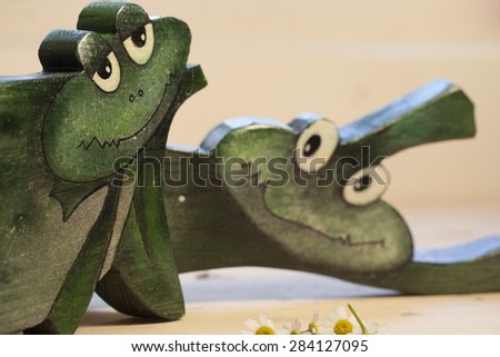 Happy frog. Toy of wood on the background of the interior with flowers