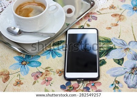 Template. Phone on the tablecloth with flowers. Against the background of a coffee cup
