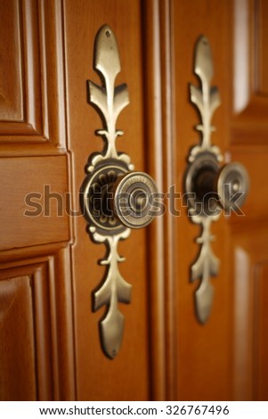 Vintage door handles on wardrobe doors of polished wood. Bronze-colour metal door handles. Carved door handle.
