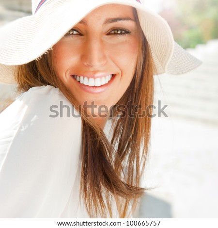 Portrait of pretty cheerful woman wearing white dress and straw hat in sunny warm weather day. Walking at summer park and smiling
