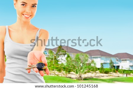 Woman holding new keys and looking at camera. Brand new modern houses on background