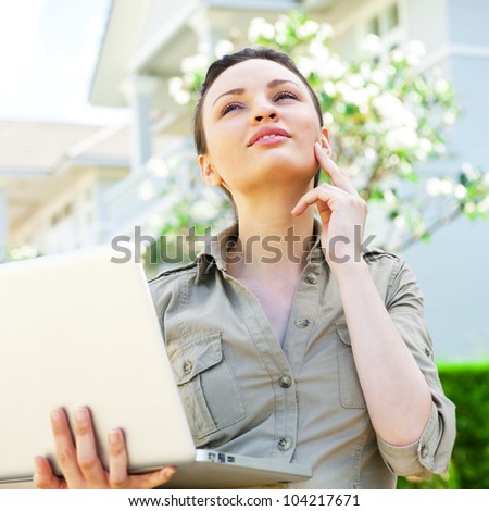 Young pretty female realty agent with laptop presenting beautiful detached house