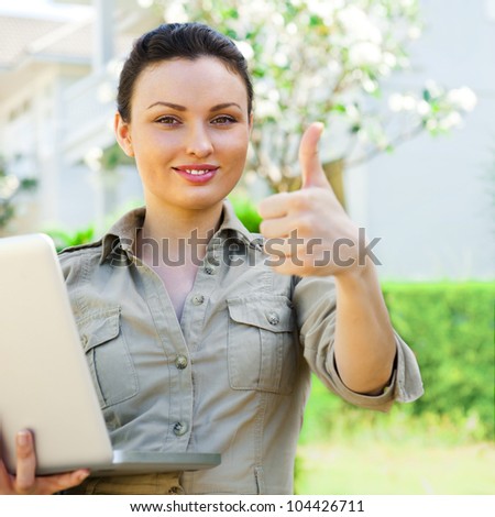 Young pretty female realty agent with laptop presenting beautiful detached house