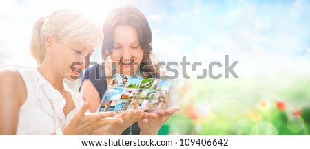Two women sitting at park and using virtual interface to watch video or pictures