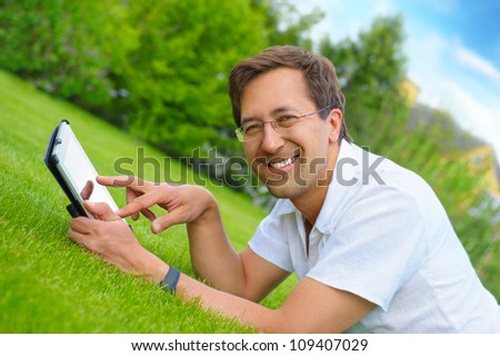 Adult man at summer park resting on weekend using his tablet computer to communicate friends or have fun with new photo, video and audio