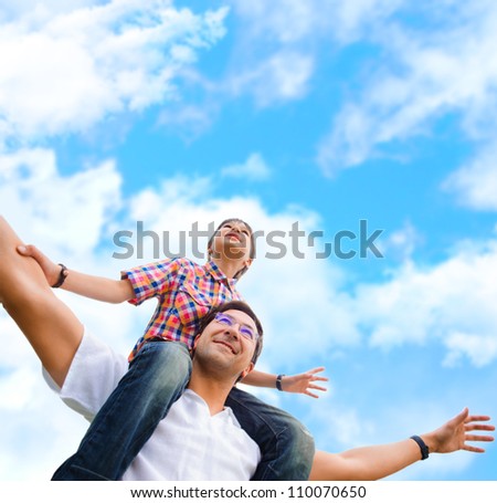 Portrait of smiling father giving his son piggyback ride outdoors against sky Portrait of smiling father giving his son piggyback ride outdoors against sky