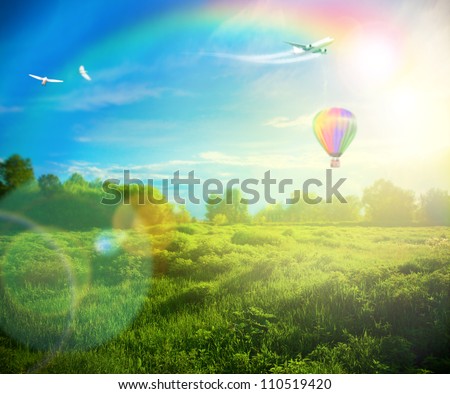 Beautiful image of stunning sunset with atmospheric clouds and sky over vibrant fields in  countryside landscape with hot air balloon, birds and airplane flying high