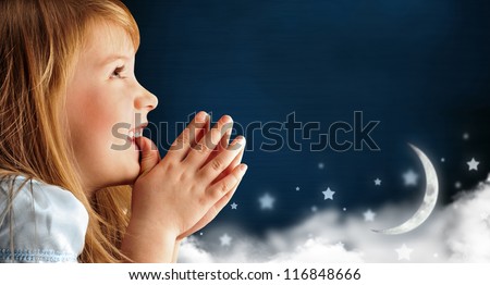 Portrait of little smiling praying girl in blue dress against dark fairy sky background with moon and stars. Lots of copyspace