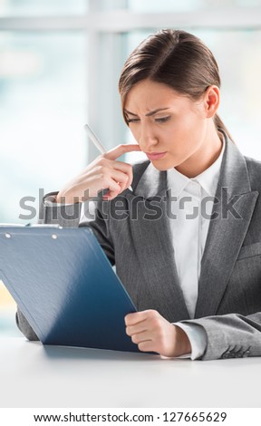 Front view of business woman looking over papers on clipboard at her office