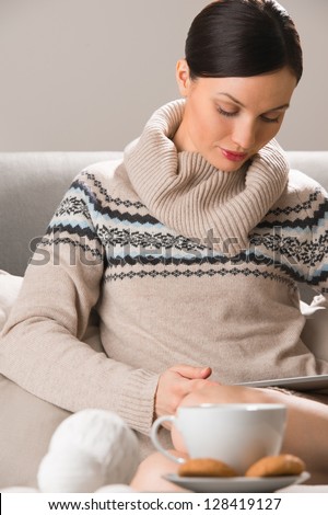 Smiling young woman using tablet computer at home at night before going to sleep. Cup of tea or coffee and cookies in front of her on table