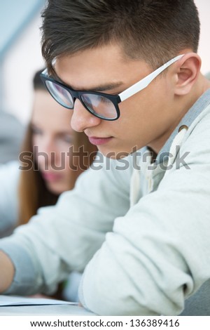 High School students. Young handsome man student sitting in classroom with his female classmate and making notes during lecture.