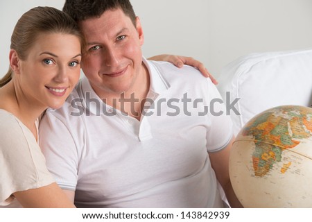 Portrait of happy romantic couple sitting together at home with globe planning their vacation and trip. Travelling concept