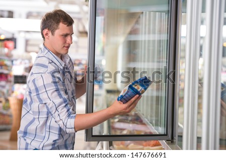 Man In A Supermarket Standing In Front Of The Freezer Looking For His Favorite Frozen Food