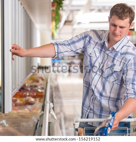 Man in a supermarket standing in front of the freezer looking for his favorite frozen food and preparing for thanksgiving dinner
