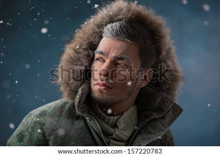 Handsome man wearing jacket with fur hood in winter snow at night