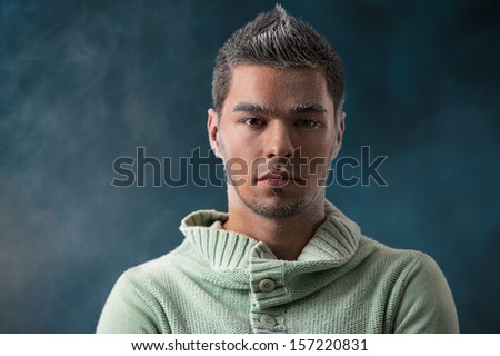 Men winter fashion. Handsome man with black hair wearing green jersey. Covered with snow. Cold. Casual look. Studio shot on smoky dark background.