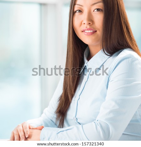 Portrait of a cheerful Business woman sitting on her desk with hands on table and  looking at camera
