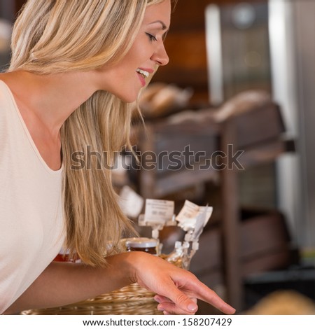 Positive young woman at the bakery store choosing what she wants to by and placing order to seller