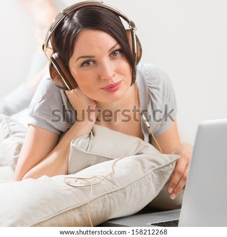 A young woman laying on the floor in front of her laptop and listening music