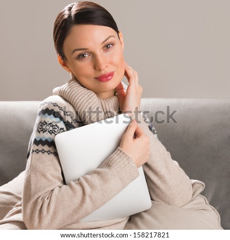 Smiling young woman using tablet computer at home at night before going to sleep. Cup of tea or coffee and cookies in front of her on table
