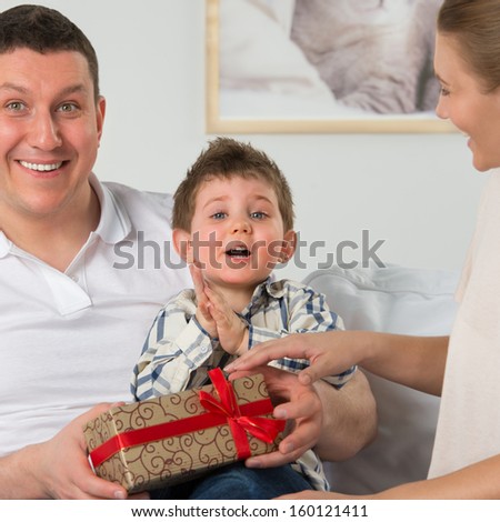 Couple giving gift to their little son in the living room. Happy family portrait