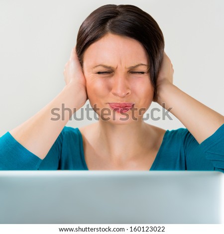 Young pretty woman with closed eyes and her covering ears sitting in front of laptop. Don\'t wants listen other opinions  and a lot of work concept