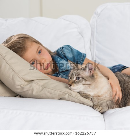 Little girl laying on sofa with her tabby cat