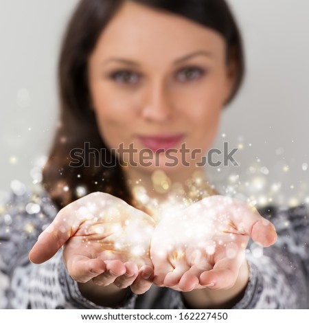 Pretty Young Brunette Woman Smiling Against Gray Background With Magic Sparkle In Her Hands Cupped Together