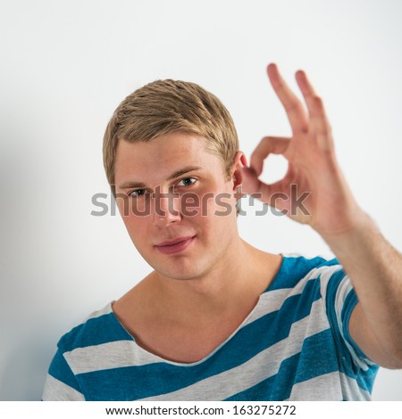 Closeup of good looking young man gesturing okay sign while leaning on white wall