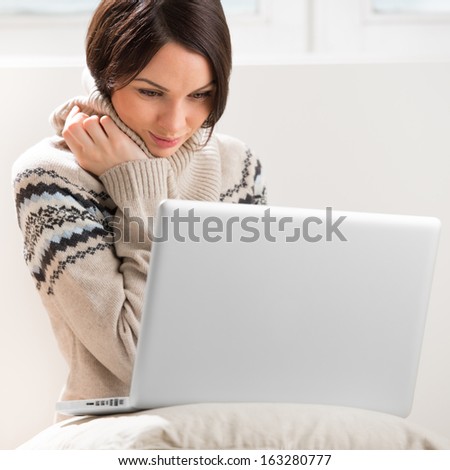 A young woman sitting on the floor in front of her laptop, looking at screen