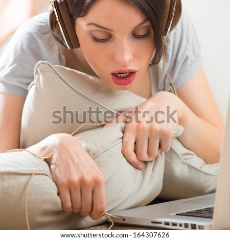 A young woman laying on the floor in front of her laptop and inserting headphones to laptop to listen music