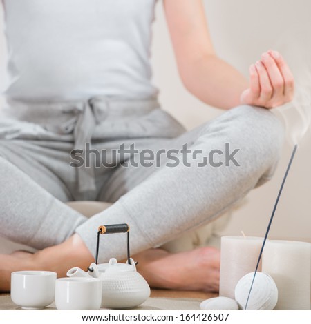 Yoga meditation at home. Relaxation concept with unrecognizable spiritual young woman sitting in front of candles, tea and aromatic sticks