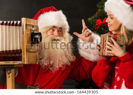 Photo of Santa Claus with his wife taking pictures with Christmas gift at home