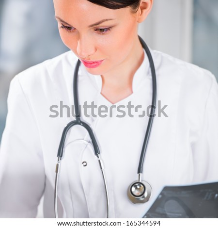 Portrait of a female doctor holding ultrasound results and using her laptop computer at clinic