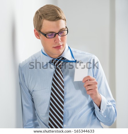 Happy smiling business man showing blank badge, while leaning on wall at office
