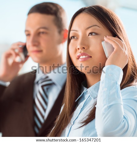 Successful business people talking on cell phone while standing at office or hallway