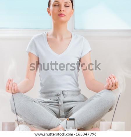 Yoga meditation at home. Relaxation concept with unrecognizable spiritual young woman sitting in front of candles, tea and aromatic sticks