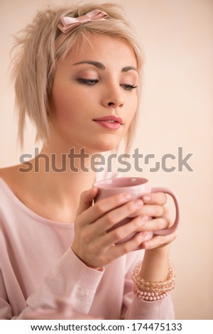 Young beautiful blond woman having tea-party. She is very satisfied. Short hair and pink colors - modern style