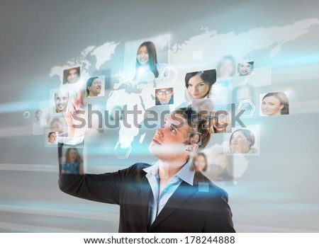 Young successful man looking at worldmap with profile photos of his colleagues and touching virtual screen. International communication concept.