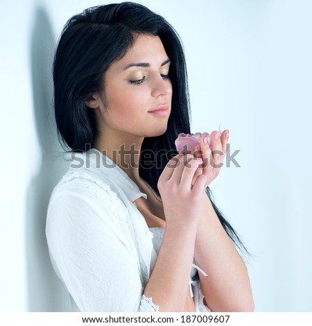 Femininity - young beautiful tender woman holding lily flower and standing near white wall