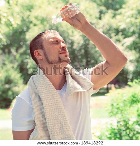 Sport fitness man. Young athletic man cooling himself from a drinks bottle outdoors at park