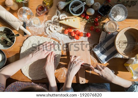Two women cooking pizza at home. Filling pizza with ingredients. Top view. Overhead view.