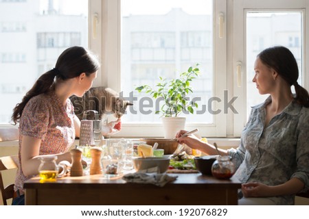Two women cooking pizza at home. Filling pizza with ingredients and feeding cute cat