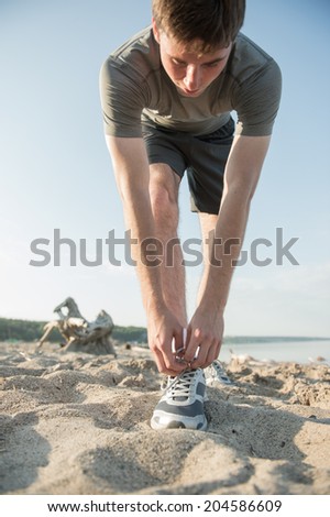 Young man is tying his shoe while running at sunny beach